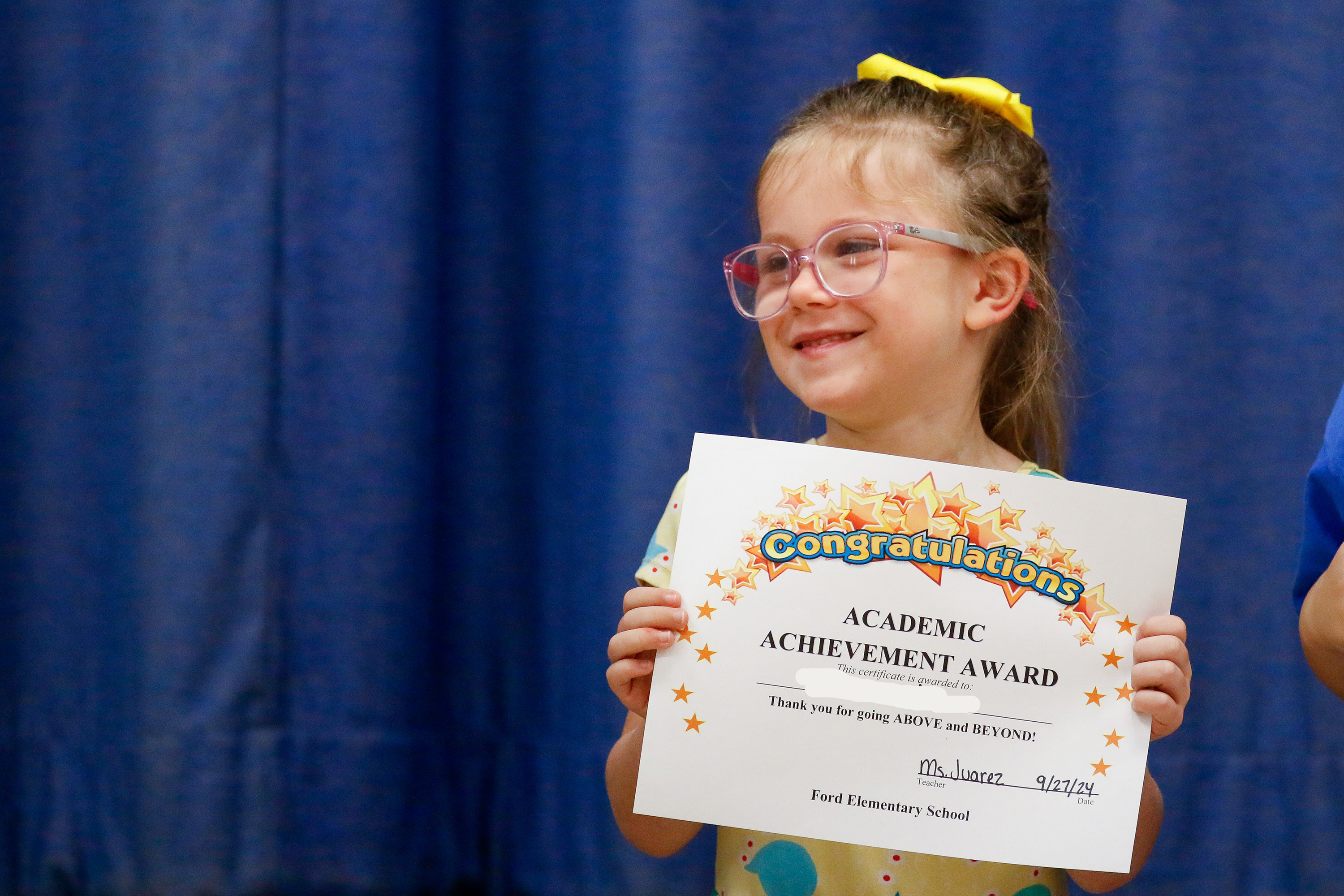 A little girl with glasses smiles with her Academic Achievement Award