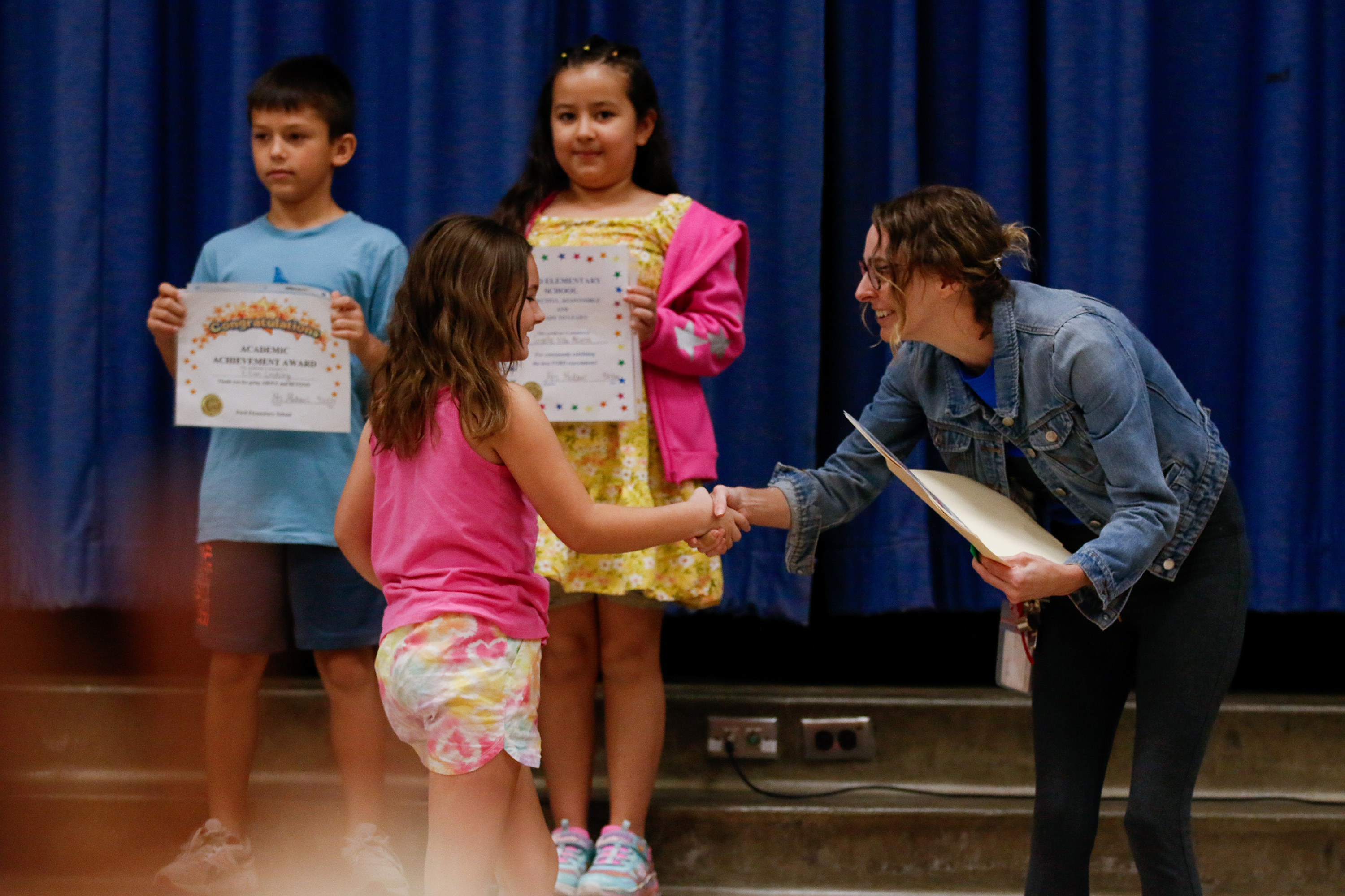 A teacher shakes a little girl's hand as she gives her an award certificate