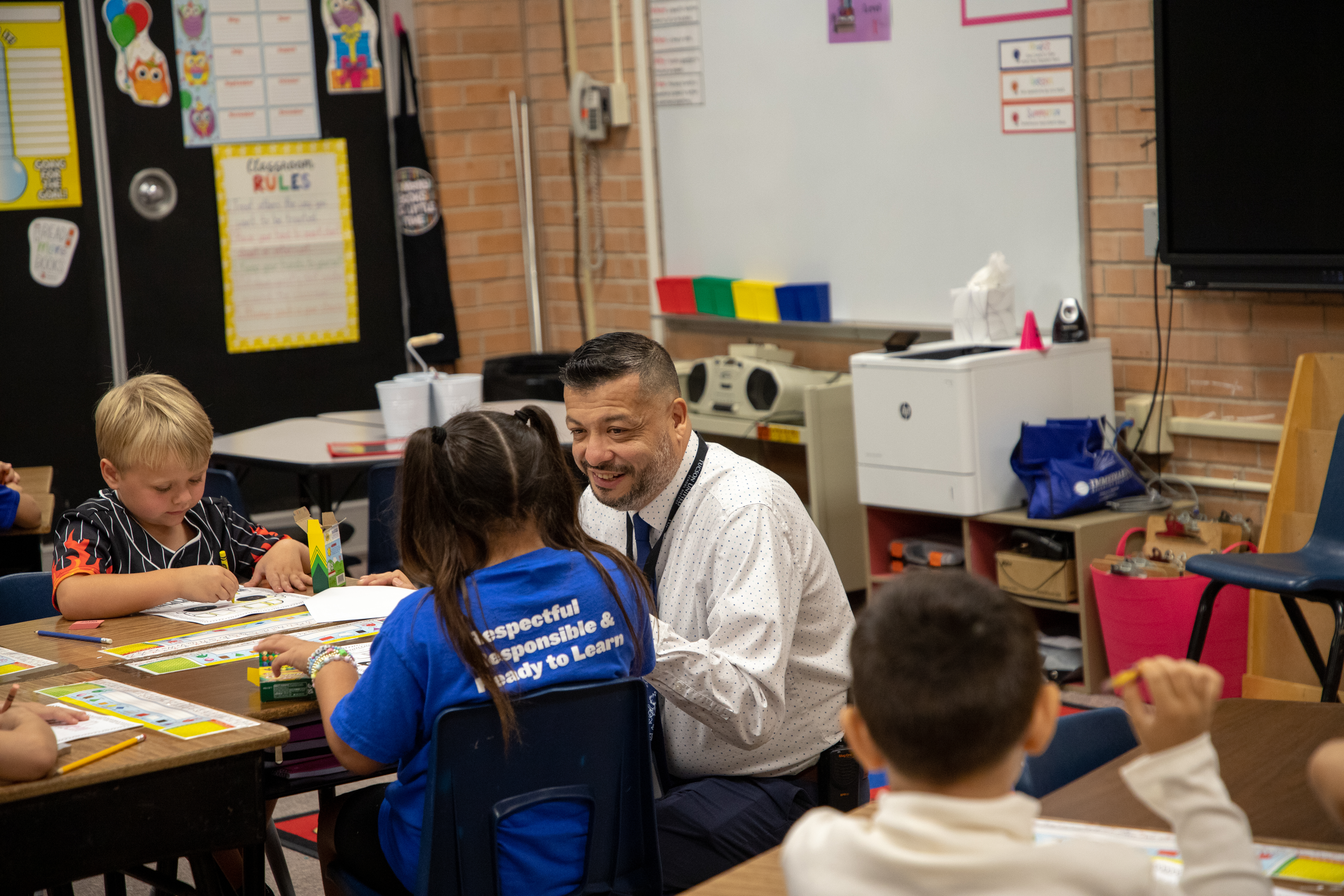 Ford's principal squats down at a desk to talk to a student