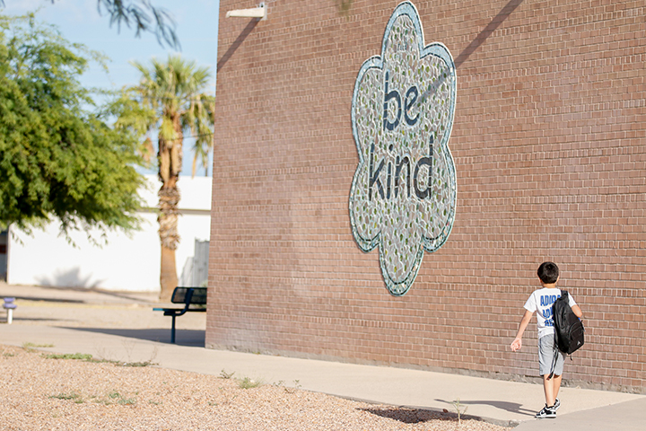A boy walks underneath the Be Kind mural