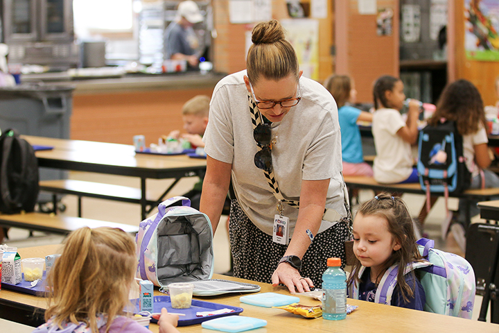A woman leans over a girl sitting at a table in the cafeteria