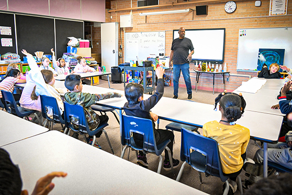Students watching a man present raise their hands