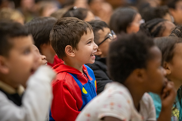 Students sit on the cafeteria floor, smiling as they watch the yo-yo show