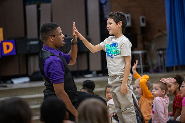 A man in a purple shirt and black vest high-fives a boy in a t-shirt